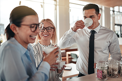Mitarbeiter stehen an einem Tresen und trinken gemeinsam Kaffee aus einer leitungsgebundenen Kaffeemaschine.
