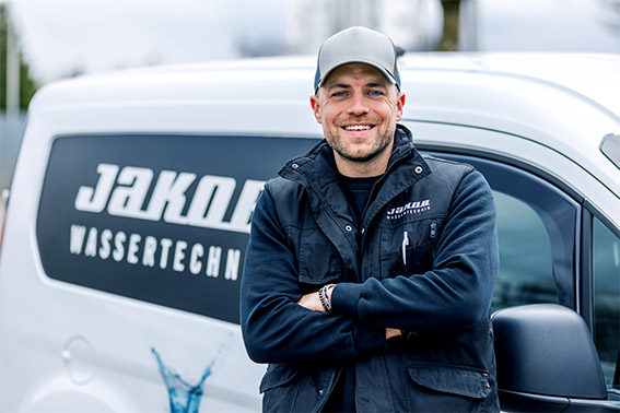 Bei Jakob Wassertechnik bekommen Sie ein herstellerunabhängiges Angebot für Ihren leitungsgebundenen Wasserspender - zur Miete, Leasing oder zum Kauf. Ein Techniker lehnt an einem Transporter von Jakob Wassertechnik. Bei uns können Sie Wasserspender kaufen oder mieten.