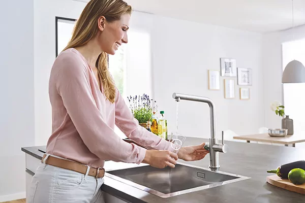 Eine Frau füllt Wasser aus dem Wasserspender Blue Professional von Grohe in ein Glas ein.