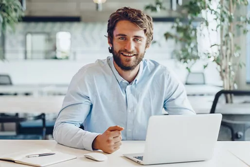 Mann vor einem Laptop, der in die Kamera lächelt.