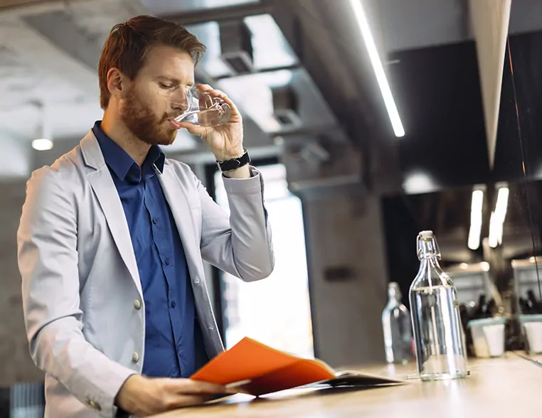 Mann trinkt Leitungswasser aus einem Glas und liest dabei in einem Dokument.