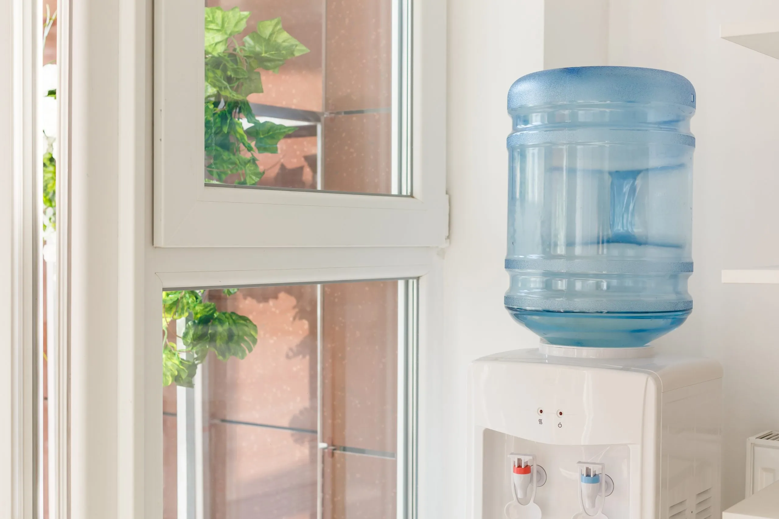 Gallonenwasserspender der neben einem Fenster steht.