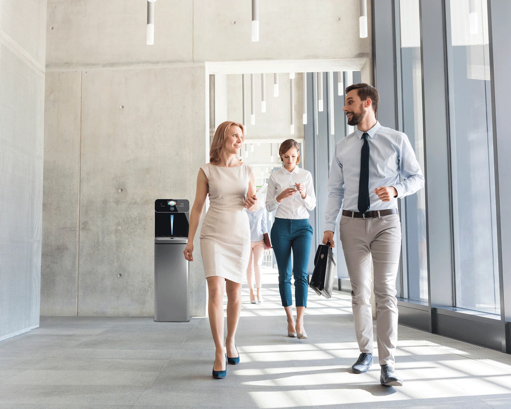 Wasserspender mieten: Flexible Versorgungslösung für moderne Büros und Unternehmen Mitarbeiter gehen durch modernes Büro mit Wasserspender – Vorteile der Miete für Unternehmen: flexibel, wartungsfrei, kalkulierbar