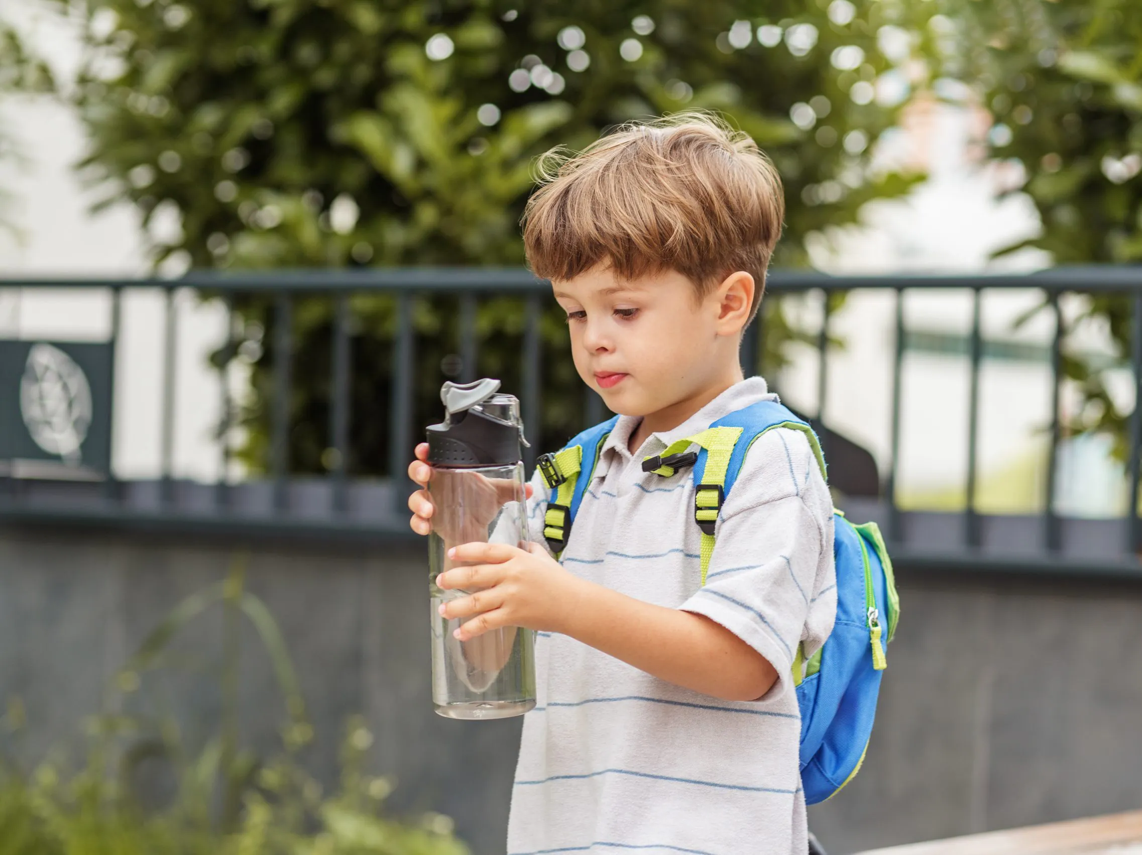 Kid boy examining water bottle outdoors. Back to school